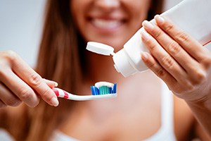 Woman applying white toothpaste to standard toothbrush