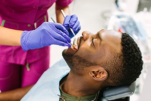 Man undergoing dental examination by dentist in pink scrubs and blue gloves