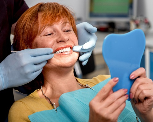 A woman looking at her dental implants in the mirror