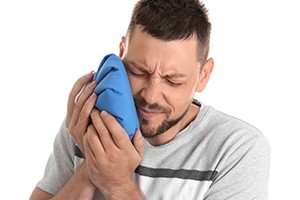 A man applying a cold compress to his face after dental implant surgery