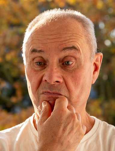 Senior man outside rubbing jaw and looking concerned